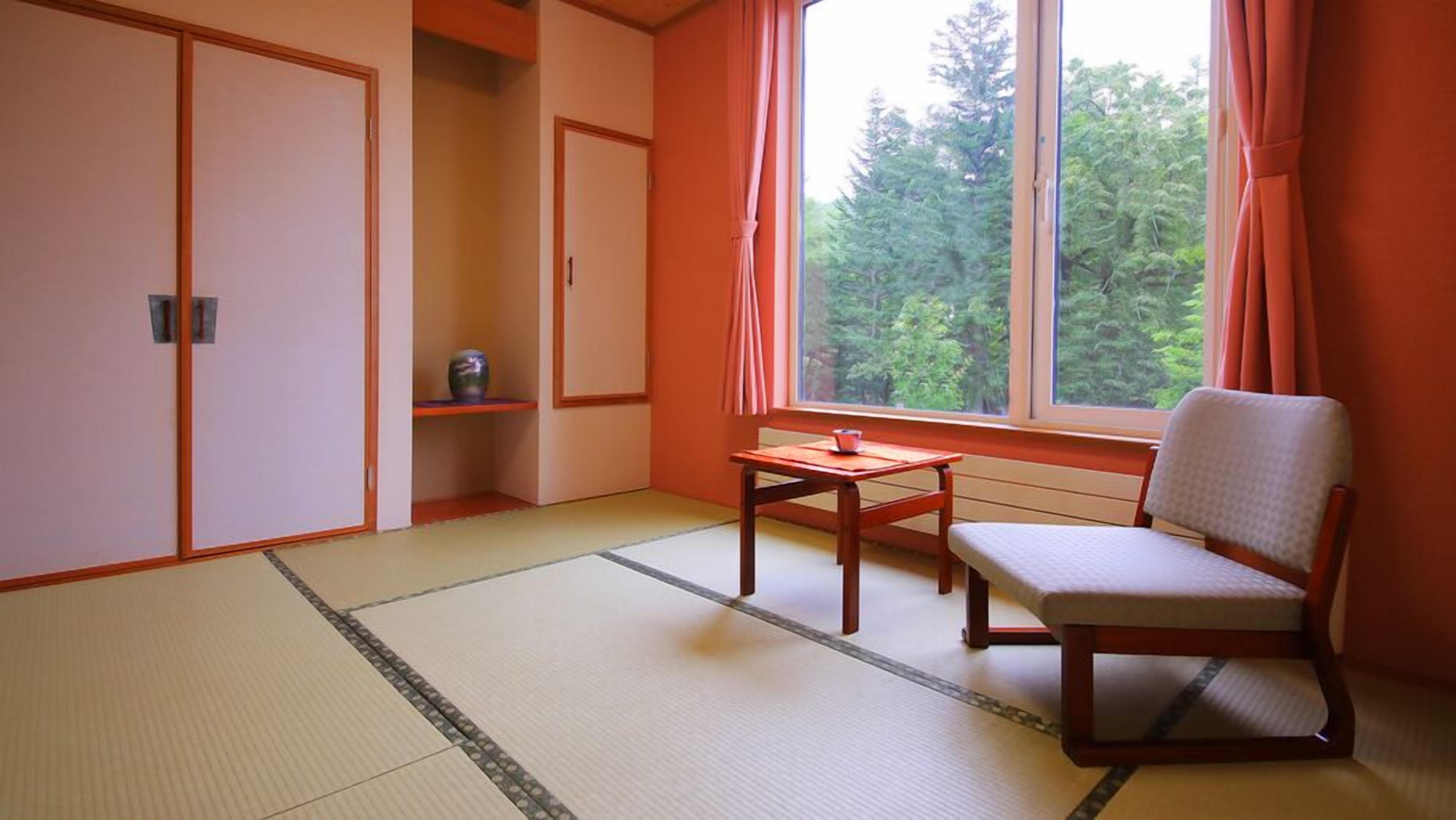 Ein Zimmer mit Tatami-Böden, einem niedrigen Tisch, einem Stuhl und einem Fenster mit Vorhängen.