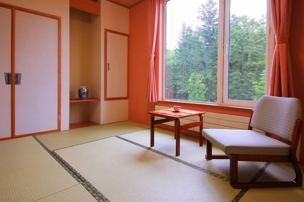 A room with tatami flooring, a low table, a chair, and a window with curtains.