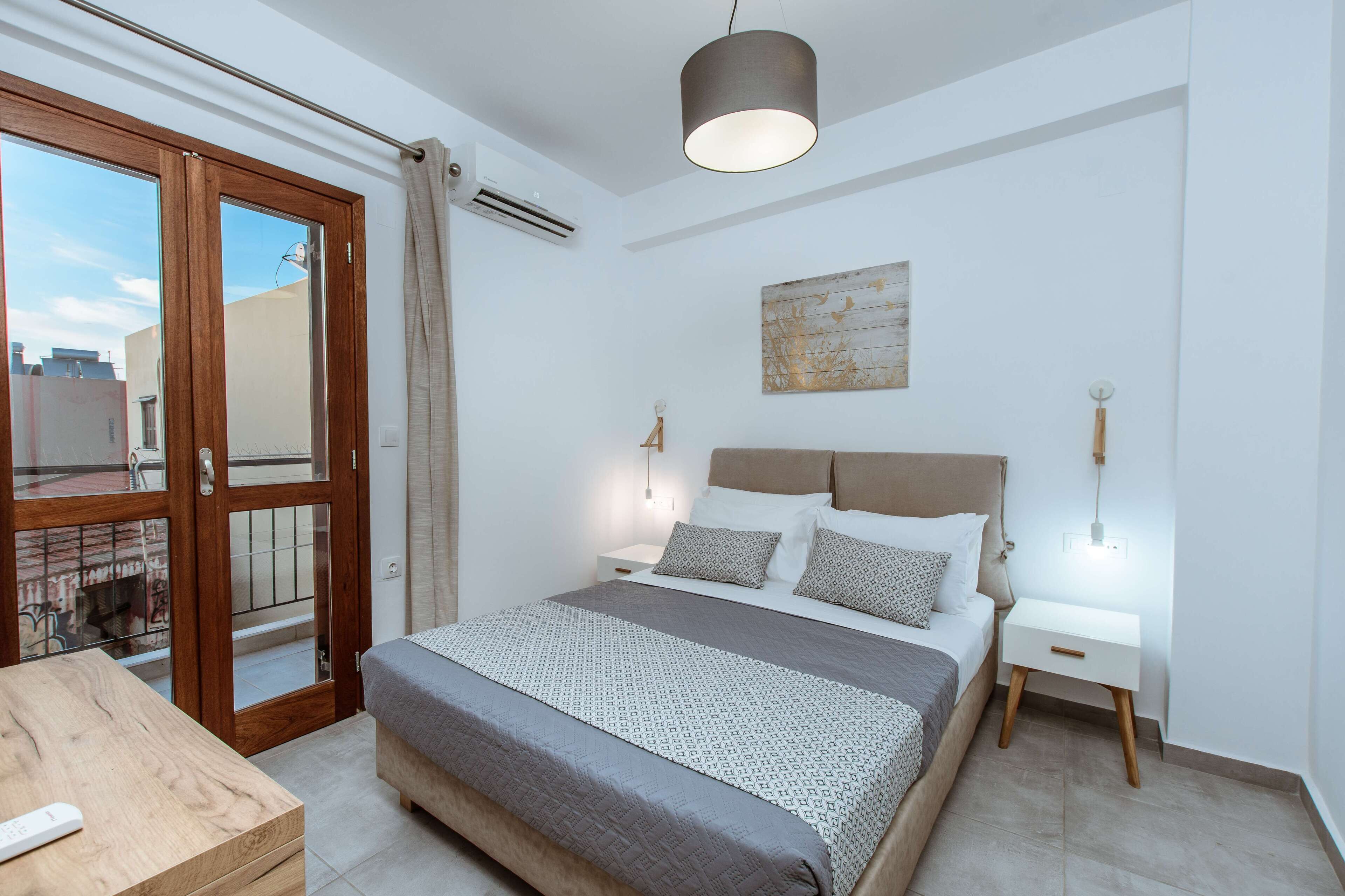 Un dormitorio con cama, mesitas de noche, una lámpara colgante y vistas a través de un ventanal.