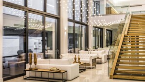 A modern hotel lobby with a staircase, large windows, and a seating area with white sofas and a coffee table. - Abaton Island Resort & Spa (Hersonissos)