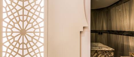 A modern bathroom with a marble sink, a decorative geometric panel, and a marble wall.