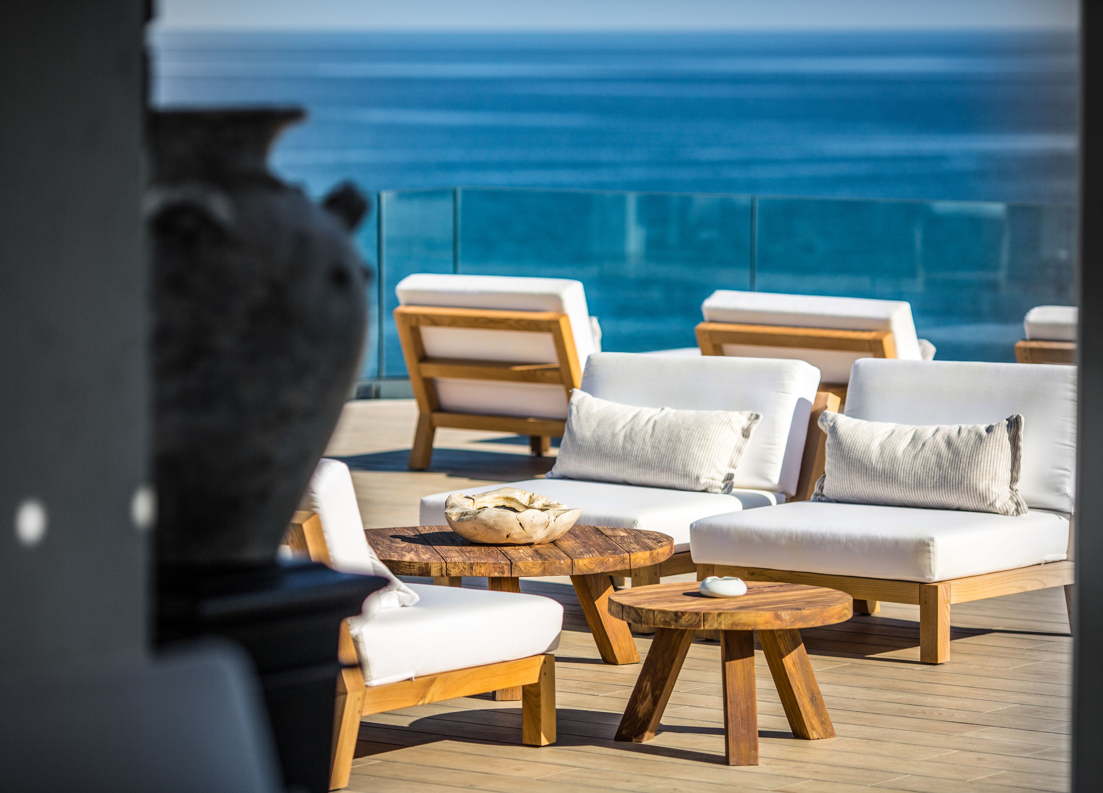 A sunlit outdoor seating area with wooden furniture and a view of the ocean.