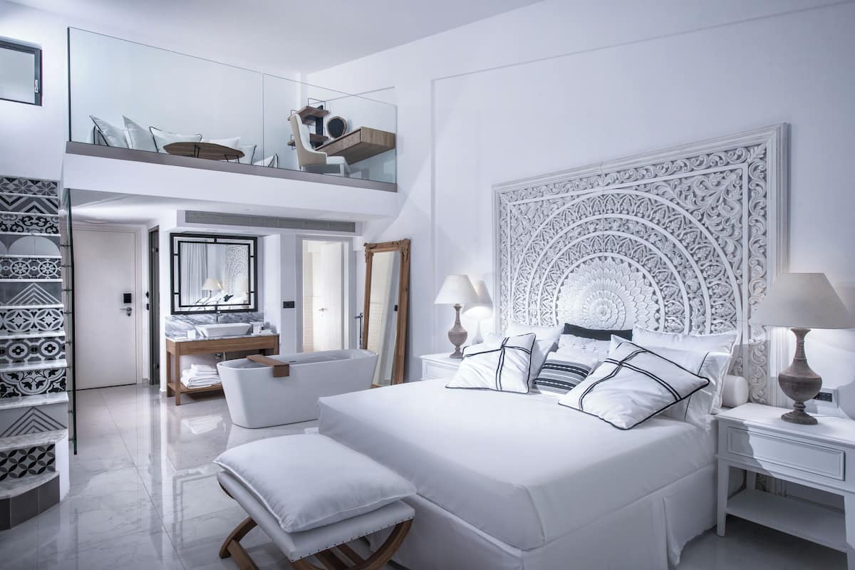 A modern bedroom with a large bed, a vanity with a mirror, and a balcony with seating.