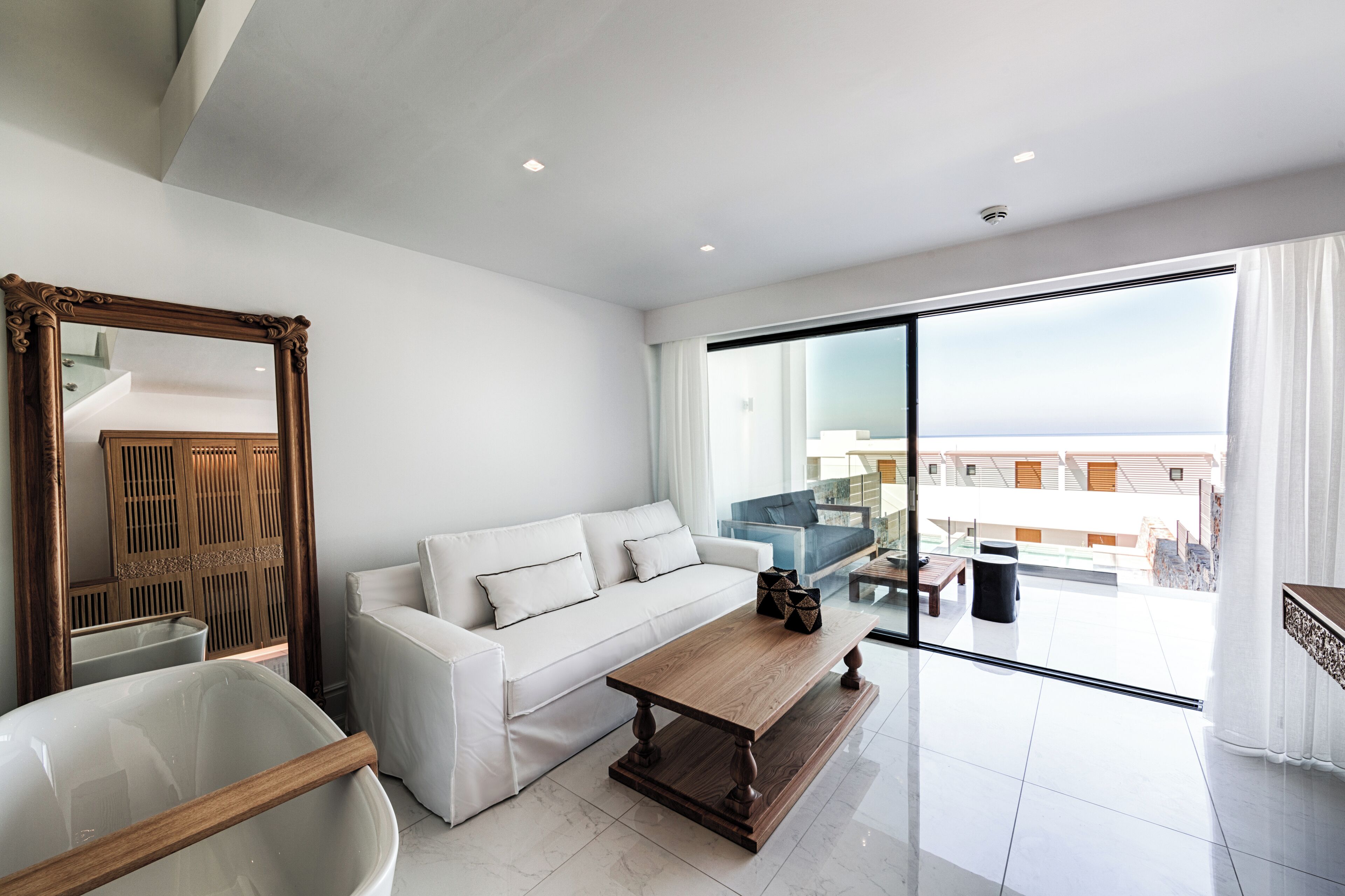 A modern living room with a white sofa, a wooden coffee table, and a large mirror.