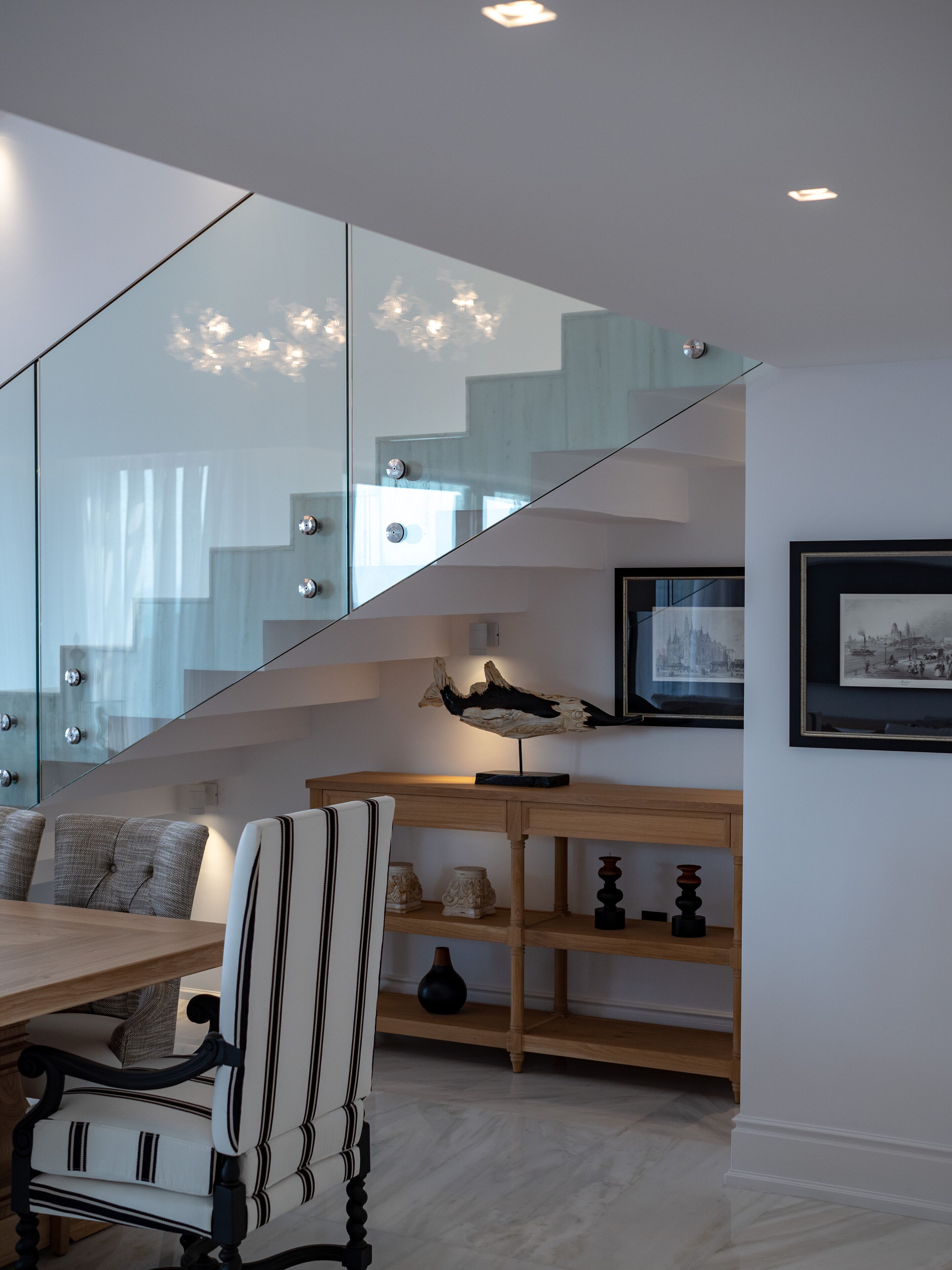 A modern interior with a dining area, a staircase, and a wall-mounted shelf with decorative items.