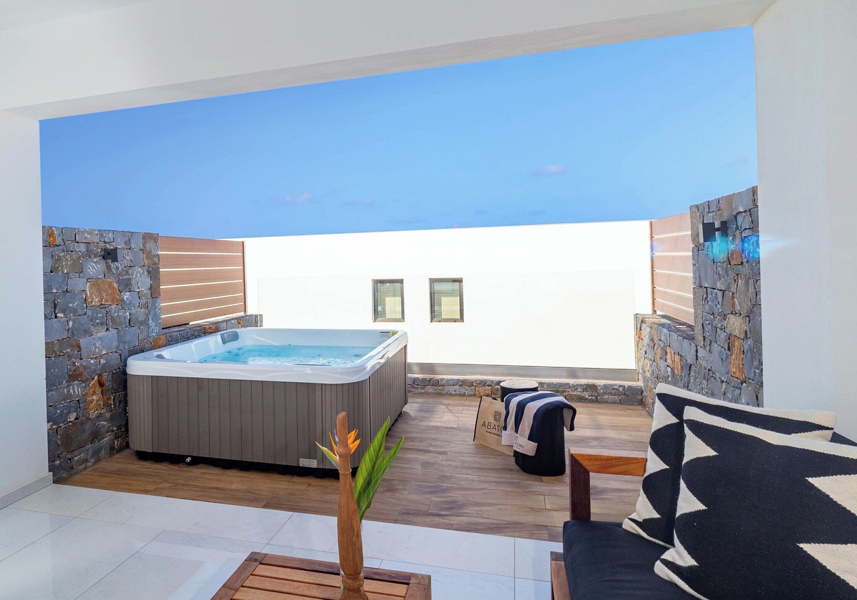 A modern outdoor patio with a hot tub, stone walls, and a view of the sky.