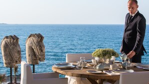 A table set for a meal with a view of the sea, a man in a suit, and two stone sculptures. - Abaton Island Resort & Spa (Hersonissos)