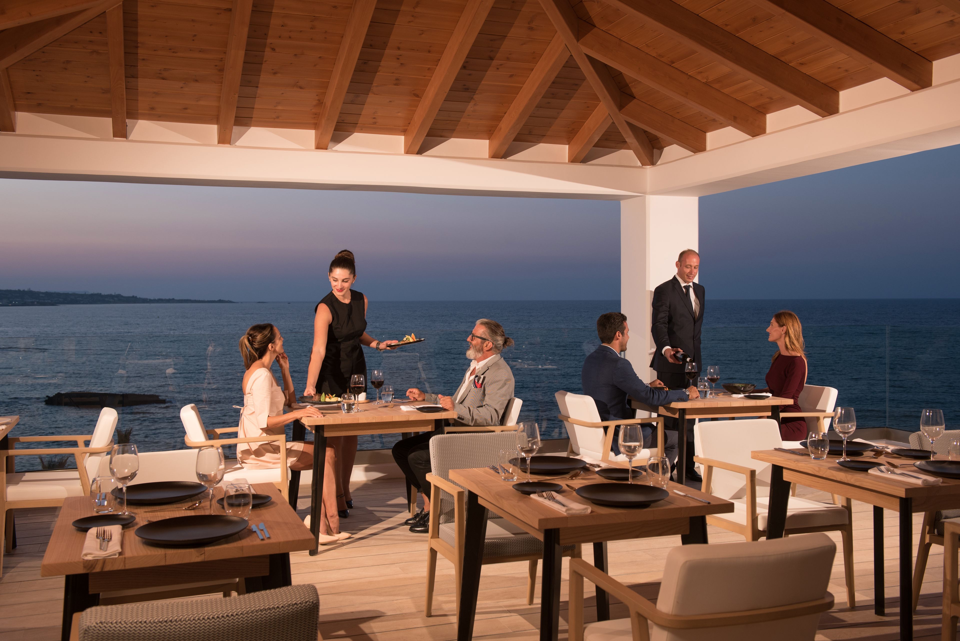 A restaurant with wooden tables and chairs, overlooking a body of water.