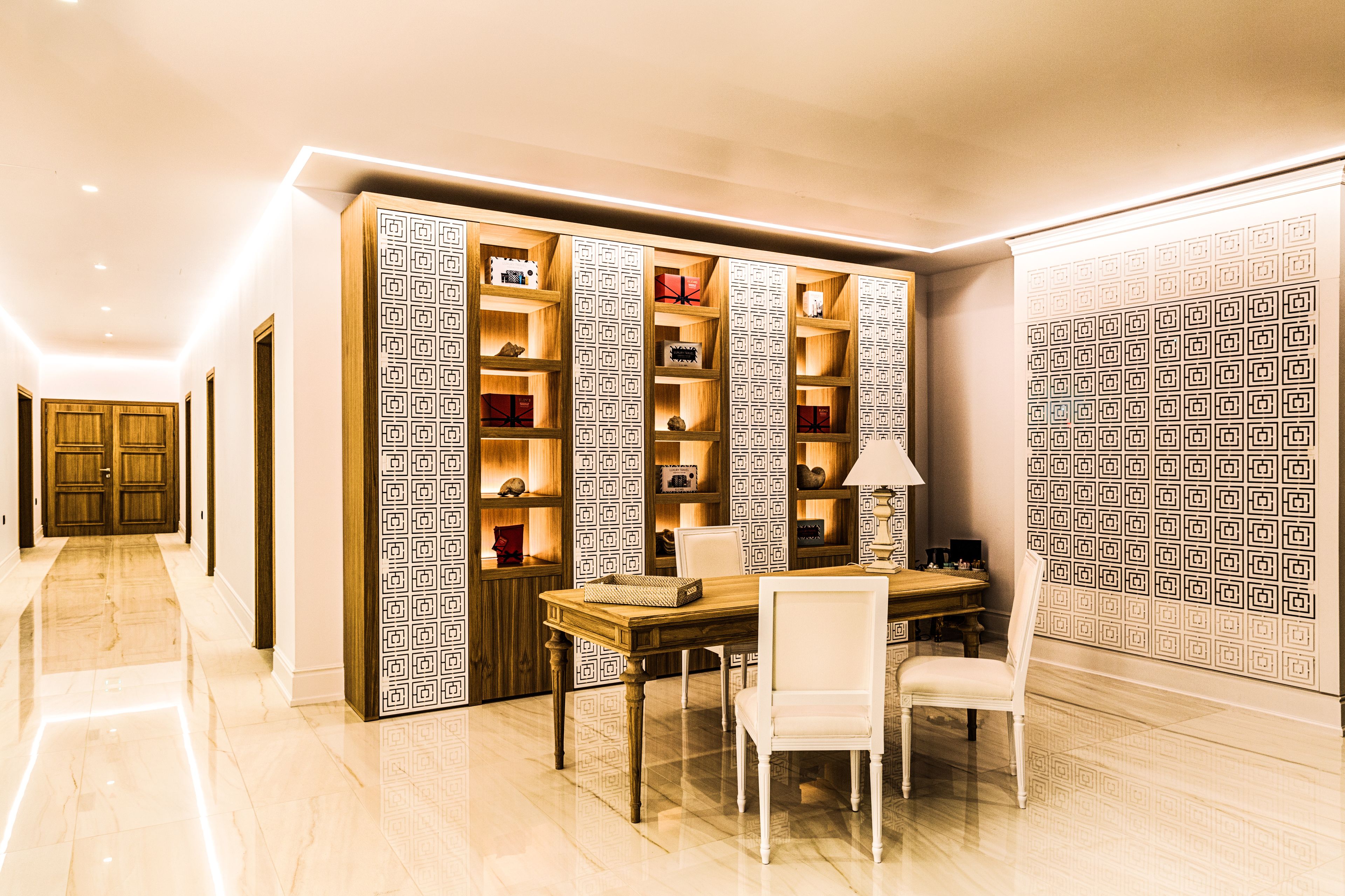 A dining area with a wooden table and chairs, a patterned bookshelf, and a lamp.