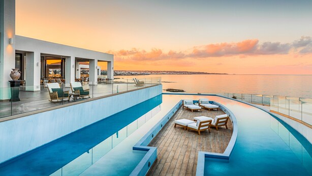 A rooftop pool area with lounge chairs and a view of the sea at sunset. - Abaton Island Resort & Spa (Hersonissos)