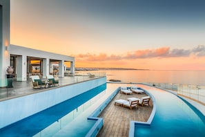 A rooftop pool area with lounge chairs and a view of the sea at sunset.