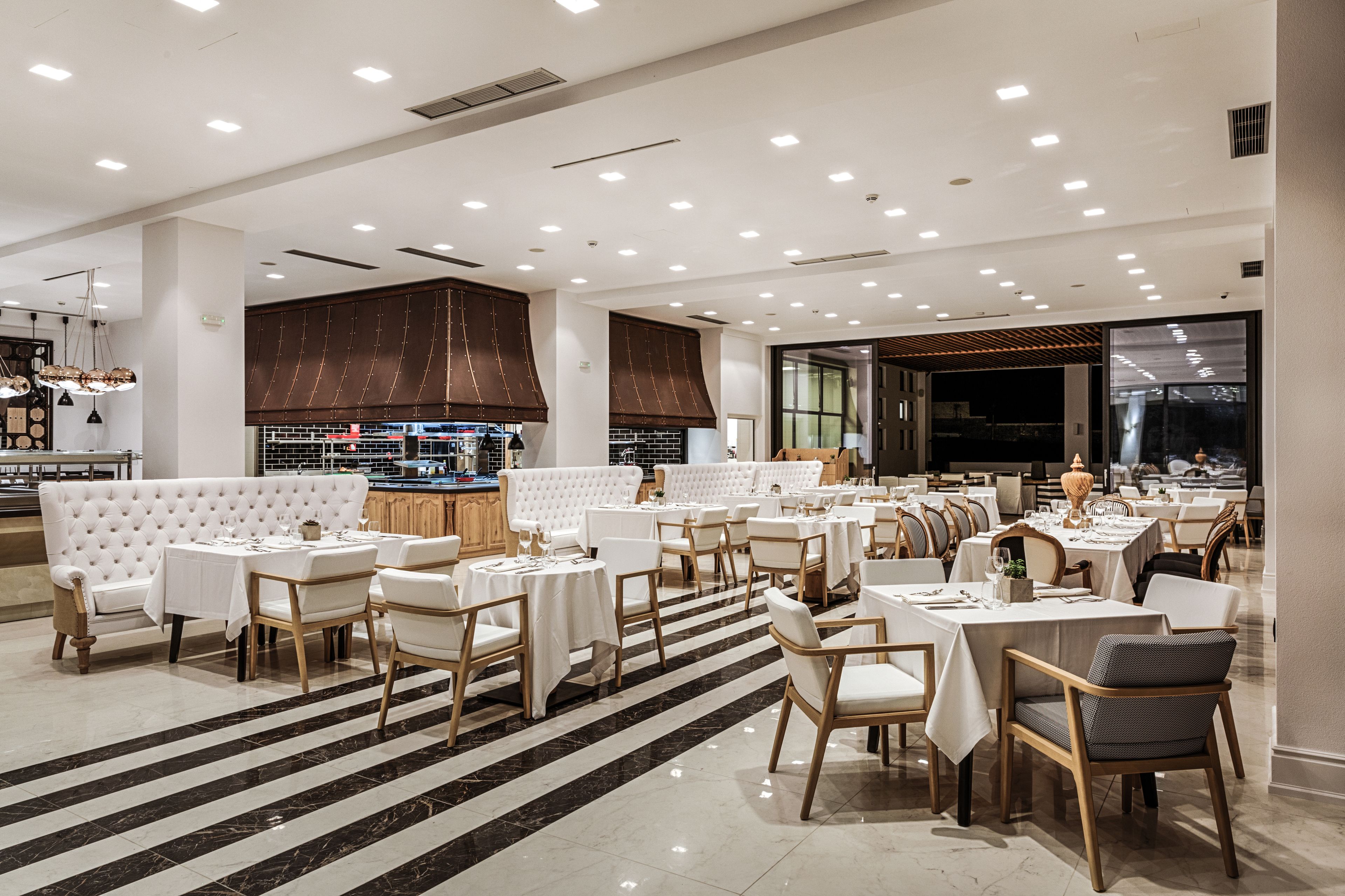 A spacious restaurant with multiple dining areas, white tables and chairs, and a modern interior design.