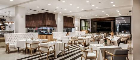 A spacious restaurant with multiple dining areas, white tables and chairs, and a modern interior design.