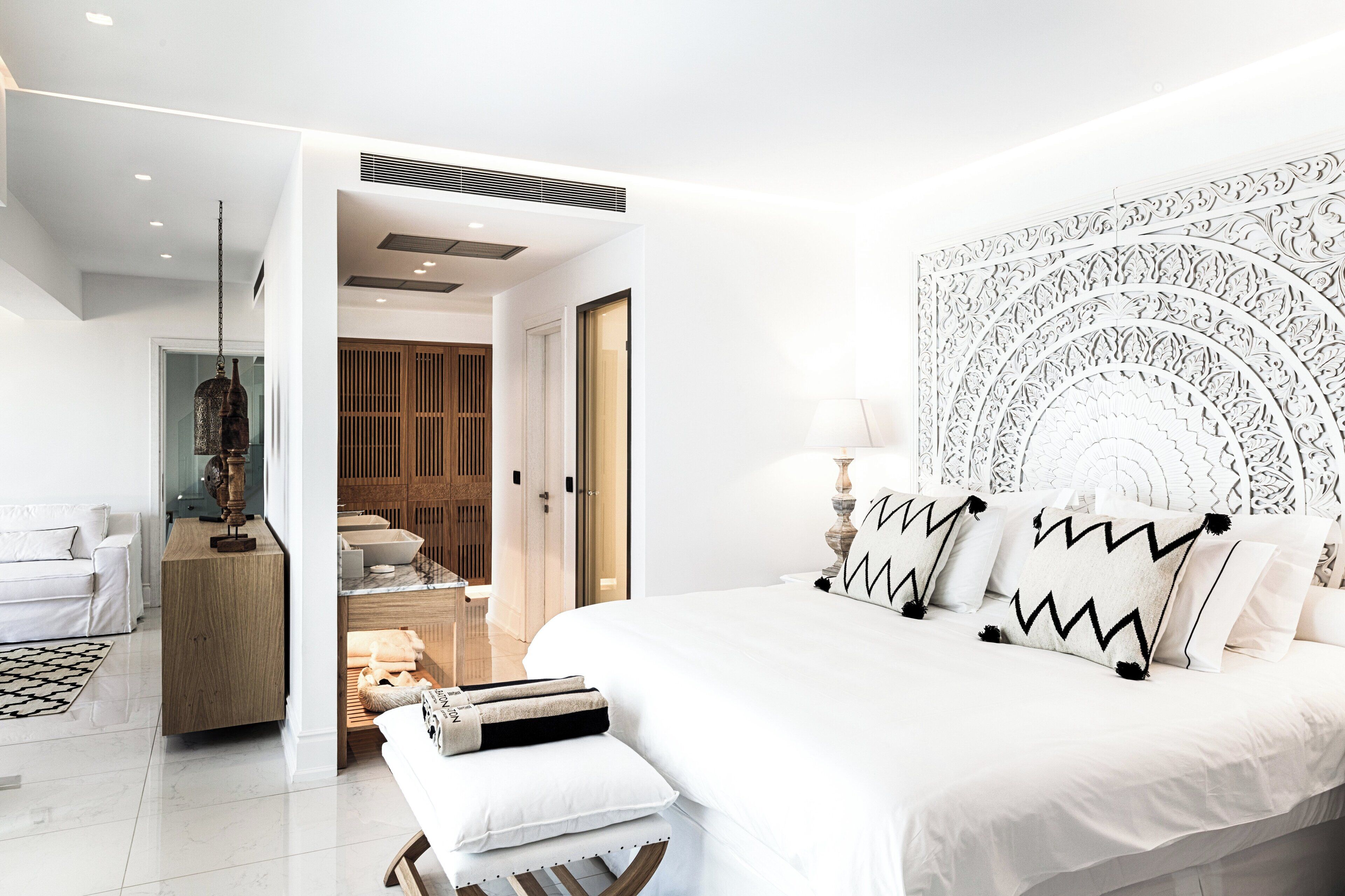 A modern bedroom with a large bed, a wooden wardrobe, and a bathroom visible through an open door.