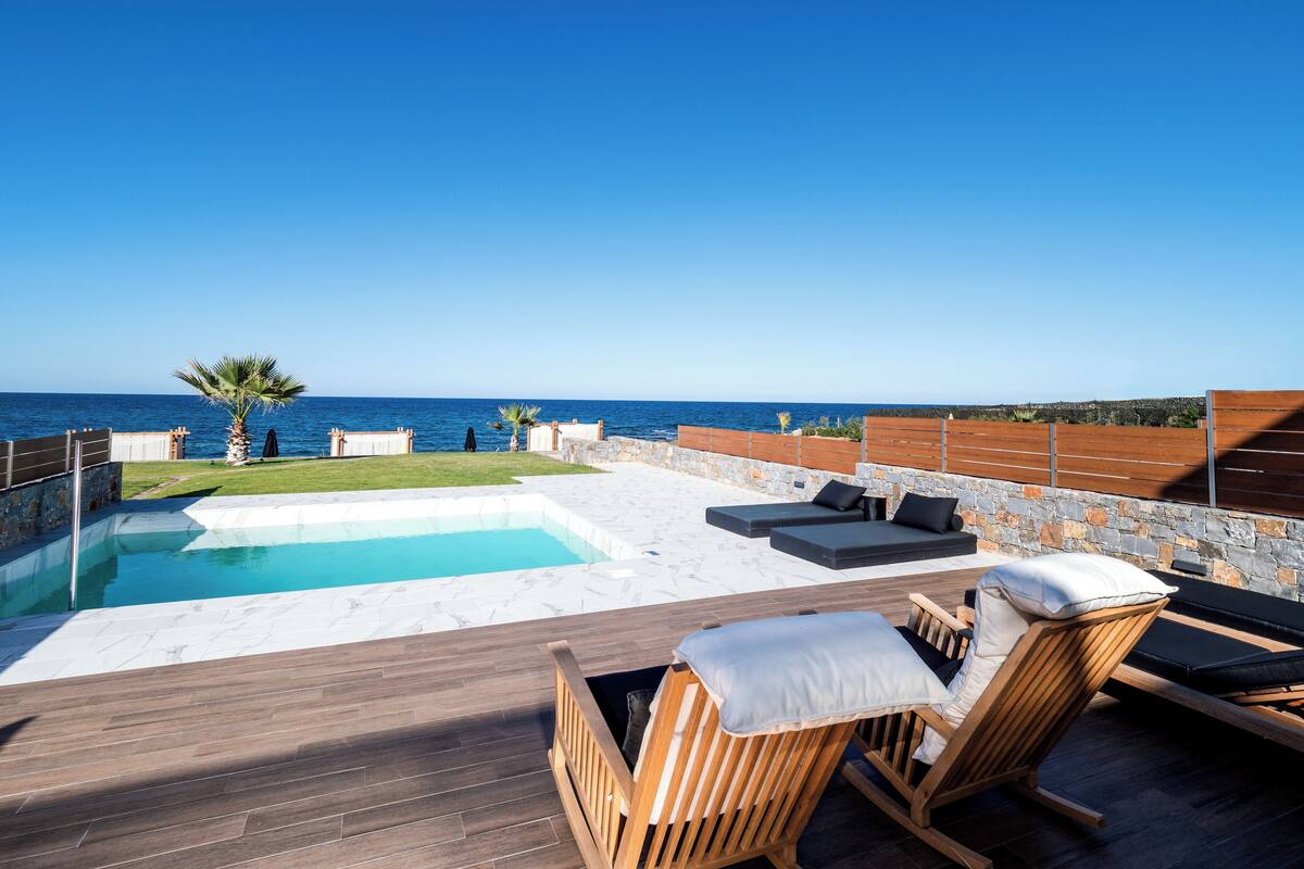A pool area with lounge chairs and a view of the sea.