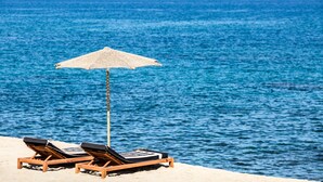 A beach with two wooden lounge chairs and a woven beach umbrella. - Abaton Island Resort & Spa (Hersonissos)