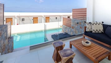 Un espace de vie extérieur moderne, doté d’une piscine, de meubles en bois et offrant une vue sur la mer.