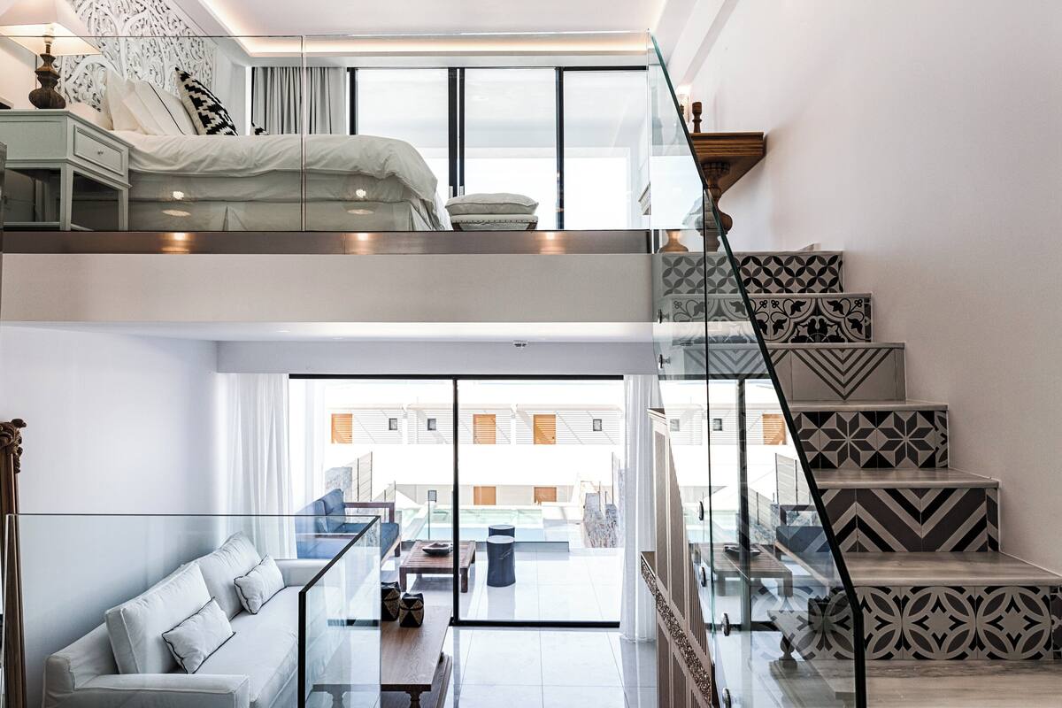 A modern interior with a glass railing, a sofa, a bed, and a staircase with patterned tiles.