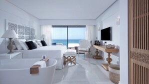 A modern hotel room with a large bed, a sitting area, a bathtub, and a view of the ocean. - Abaton Island Resort & Spa (Hersonissos)