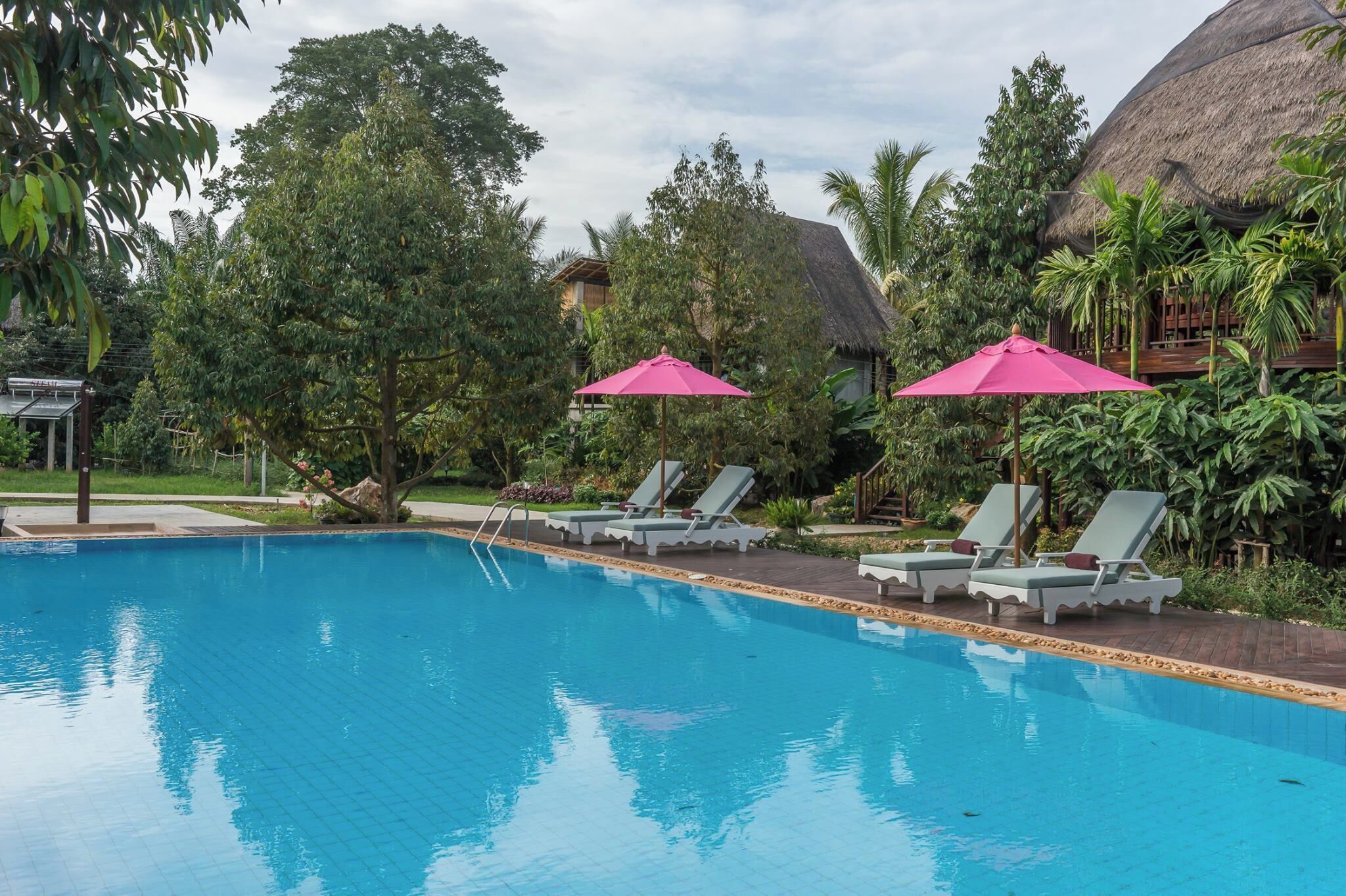 A swimming pool with lounge chairs and a thatched-roof structure.