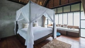Een slaapkamer met een hemelbed, een raamzitje met kussens, en een rieten dak.