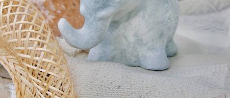 A decorative elephant figurine on a textured surface, accompanied by a wicker basket and a vase with blue flowers.