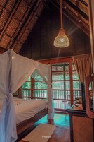 Habitación con cama bajo un dosel, lámpara colgante y vista a zonas verdes a través de amplios ventanales.