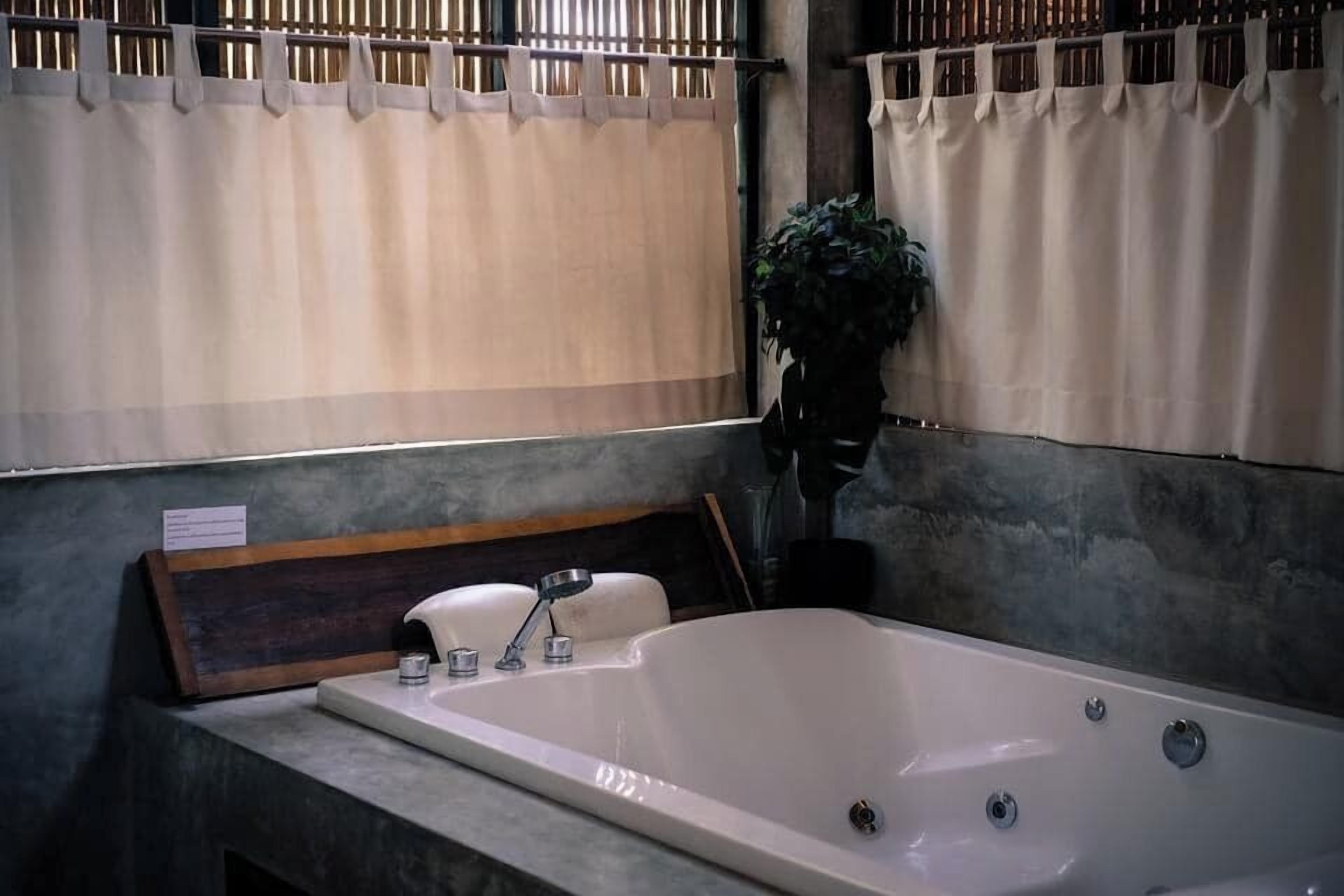 Ein Badezimmer mit einer großen Badewanne, einer hölzernen Sitzbank und einer Zimmerpflanze.