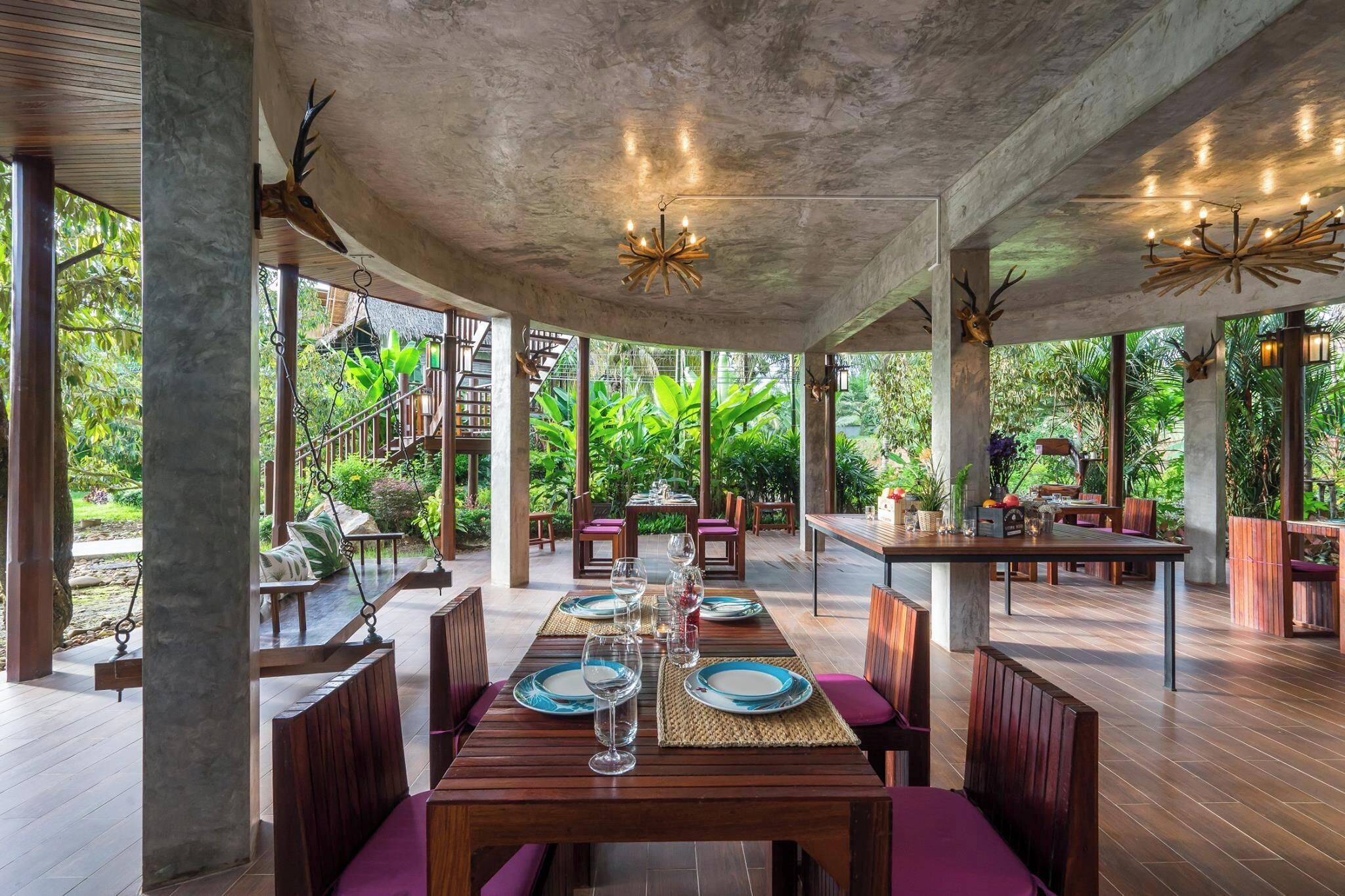 Un área de comedor al aire libre con mesas dispuestas para dos, rodeada de sillas de madera y bancos acolchados.