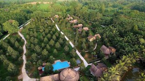 Luchtbeeld van een resort met een centraal zwembad, omringd door weelderige begroeiing en palmbomen, met meerdere accommodaties in de vorm van bungalows.