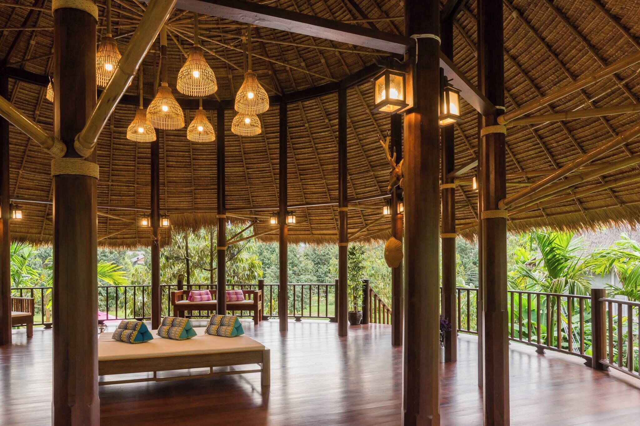 A spacious, open-air lounge with a thatched roof, wooden pillars, and hanging wicker lamps.