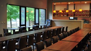 A spacious indoor dining area with long wooden tables and chairs, large windows offering a view of trees, and a bar area with hanging orange pendant lights. - One City One Vacation Farm (Nantou)