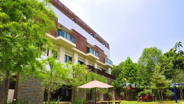 A modern building with a stone facade, multiple balconies, and outdoor seating areas with picnic tables and umbrellas. - One City One Vacation Farm (Nantou)