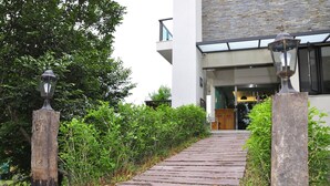 A pathway leading to a modern building with a glass entrance and a wooden door. - One City One Vacation Farm (Nantou)
