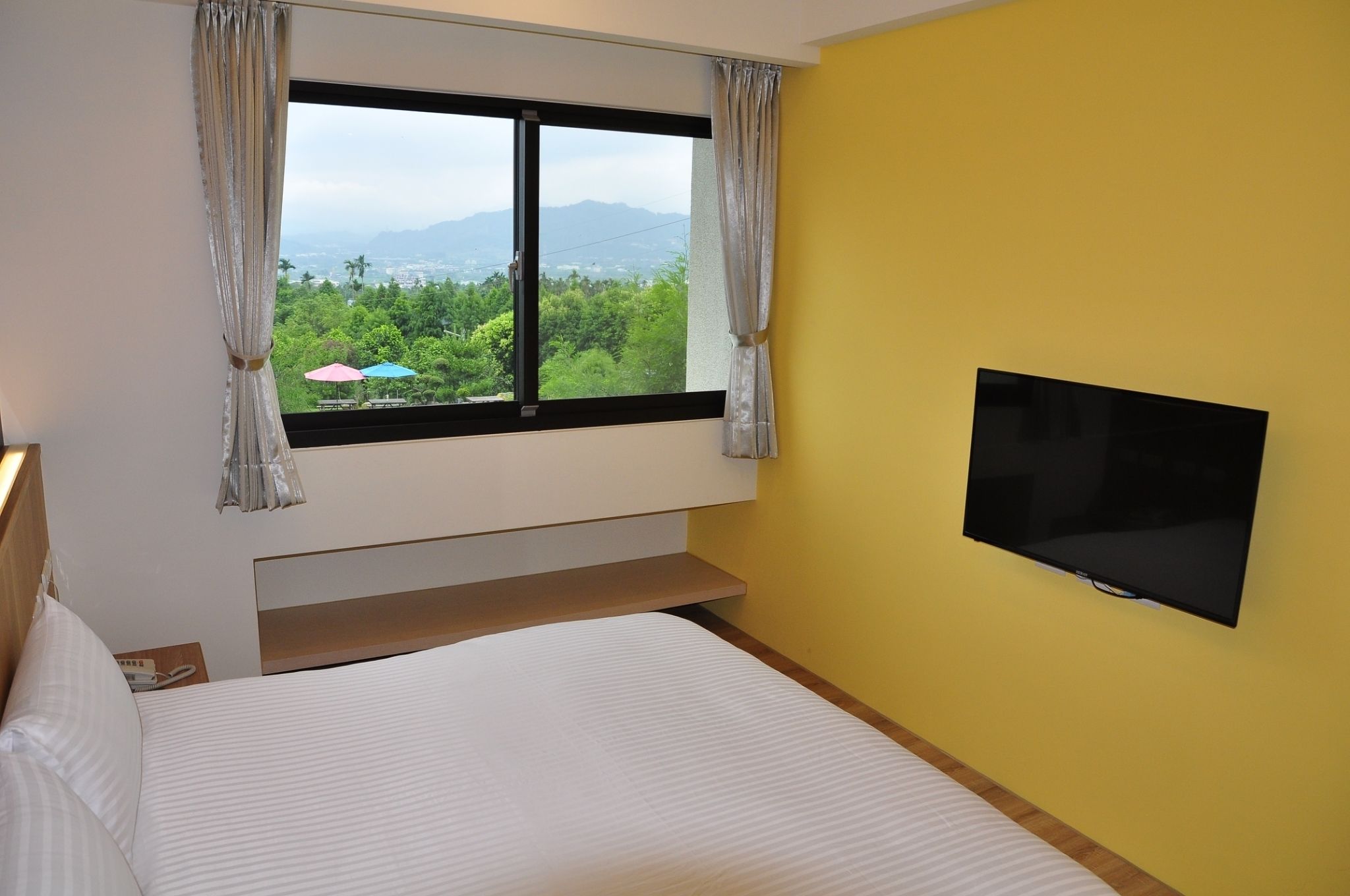 A hotel room with a bed, a TV mounted on the wall, and a window with curtains.