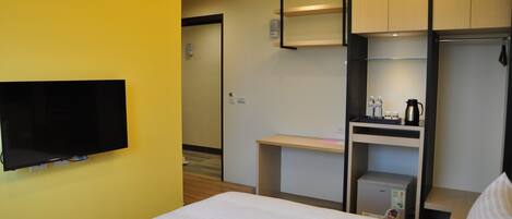 A hotel room with a bed, a flat-screen TV mounted on the wall, a desk with a coffee maker, and a small refrigerator.