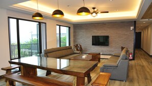A modern living room with a glass-top dining table, wooden benches, a grey sofa, and a flat-screen TV mounted on a brick wall. - One City One Vacation Farm (Nantou)