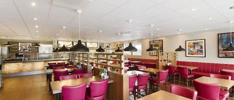 Un restaurante con mesas de madera y sillas rojas, una barra con el menú y obras de arte en las paredes.