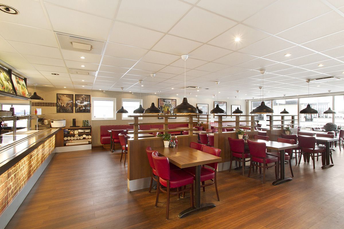 Un restaurant spacieux doté d’un plancher en bois, de sièges rouges et d’un éclairage suspendu.