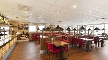 Un restaurant spacieux doté d’un plancher en bois, de sièges rouges et d’un éclairage suspendu.