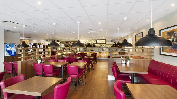 A spacious restaurant with wooden tables and red chairs, a kitchen area, and a seating area with a red sofa. - Drive-in Motell (Mjolby)