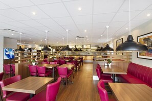 A spacious restaurant with wooden tables and red chairs, a kitchen area, and a seating area with a red sofa. - Drive-in Motell (Mjolby)