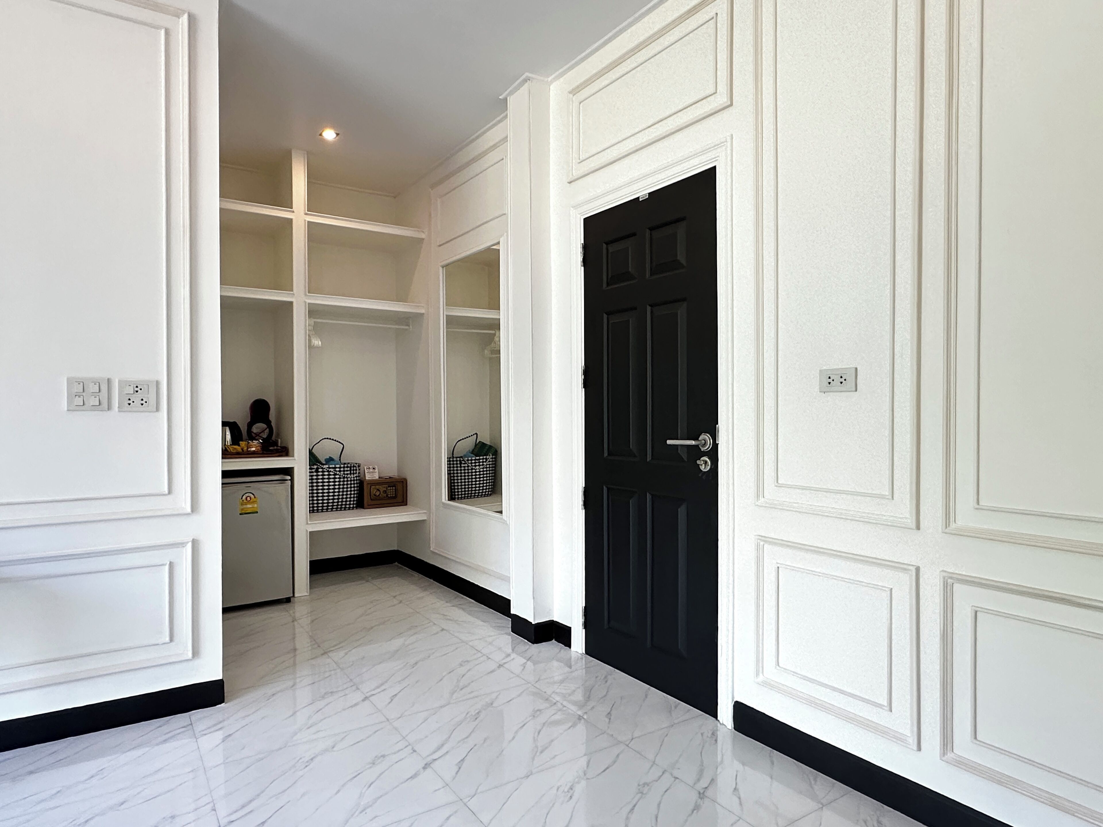 A hallway with white walls, a black door, and marble flooring.