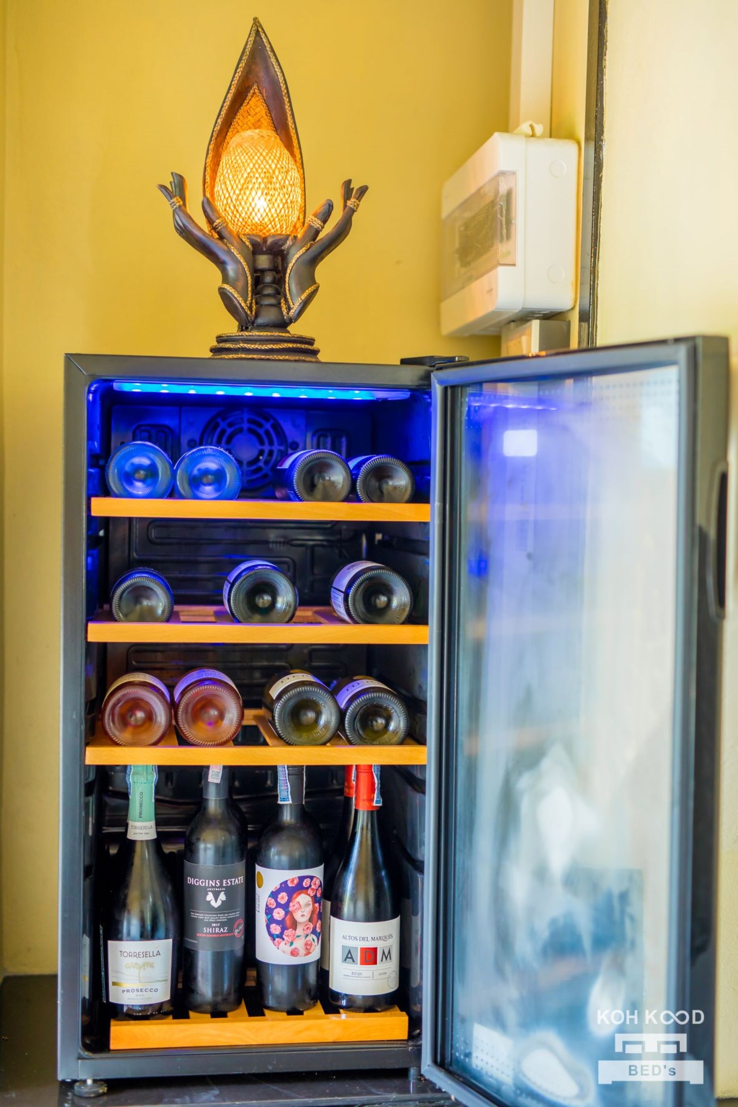 Un minibar con una lámpara decorativa, estantes con botellas y una puerta de vidrio.