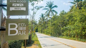 A sign for 'Koh Kood Bed's' and 'Bed's Bar' along a road with palm trees and greenery. - Koh Kood BED's (Ko Kood)