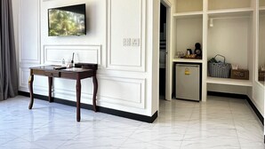 A hotel room with a flat-screen TV mounted on the wall, a small table with a chair, a minibar, and a shelf with a bag and a radio. - Koh Kood BED's (Ko Kood)