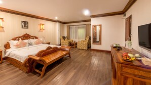 A hotel room with a wooden bed, two armchairs, a small table, a TV, and a fruit basket on a wooden dresser. - Chayra Angkor Hotel (Siem Reap)