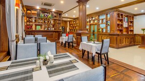 A restaurant with multiple tables, chairs, and a bar area with shelves of bottles and glasses. - Chayra Angkor Hotel (Siem Reap)