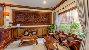 A traditional wooden interior with a large carved panel, wooden furniture, and a view through a window. - Chayra Angkor Hotel (Siem Reap)