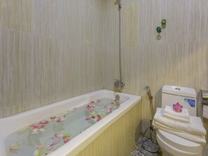 A bathroom with a bathtub filled with water and rose petals, a toilet, and a shower area.